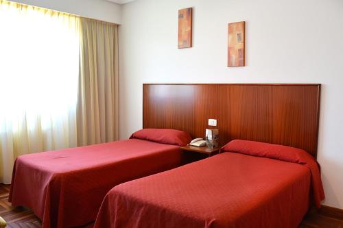 two beds in a hotel room with red sheets at Hotel Os Caracoles in Pereiro de Aguiar
