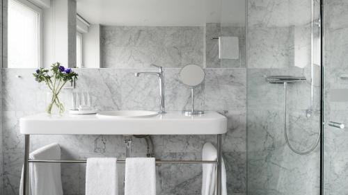 uma casa de banho branca com um lavatório e um chuveiro em Nobis Hotel Stockholm, a Member of Design Hotels™ em Estocolmo