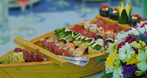 a wooden box filled with sushi on a table with flowers at Marina Frapa Resort Rogoznica in Rogoznica