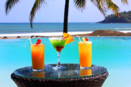 three cocktails sitting on a table next to the ocean at Playa Venao Hotel Resort in Playa Venao