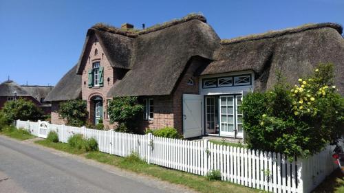 a thatch roof house with a white fence at Das Rosenhaus in Utersum