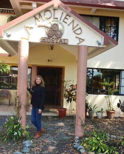 a woman standing in front of a sign for a motel at Hostal La Molienda in Puyo