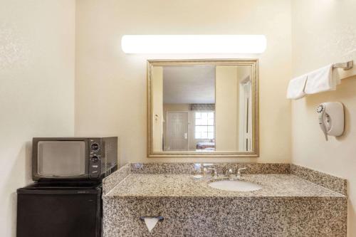 a bathroom with a sink and a mirror and a television at Days Inn by Wyndham Yazoo City in Yazoo City