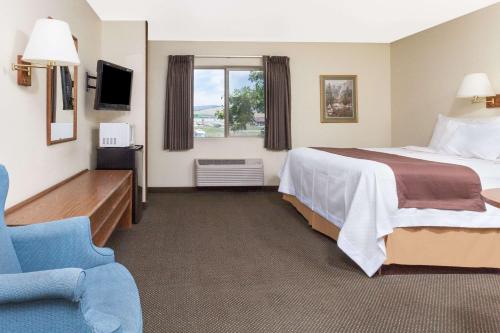 a hotel room with a bed and a blue chair at Days Inn by Wyndham Missoula Airport in Wye