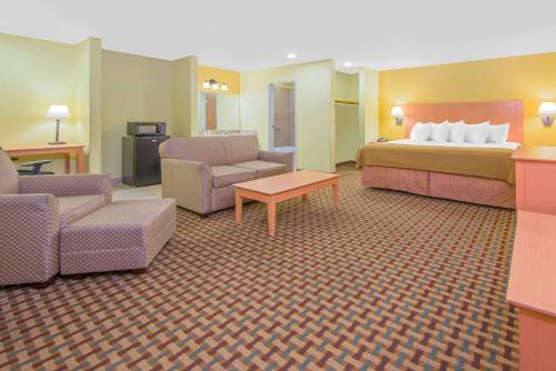 a hotel room with a bed and a couch and chairs at Days Inn by Wyndham Lubbock South in Lubbock
