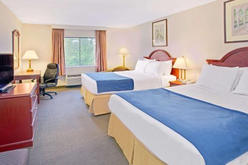 a hotel room with two beds and a desk at Days Inn & Suites by Wyndham Laurel Near Fort Meade in Laurel