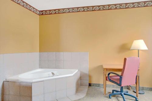 y baño con bañera, silla y mesa. en Days Inn by Wyndham Lehi, en Lehi