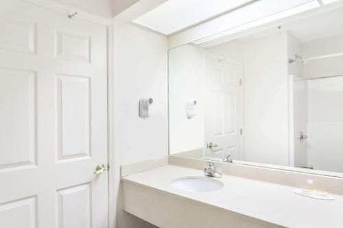 Baño blanco con lavabo y espejo en Days Inn & Suites by Wyndham Huntsville, en Huntsville