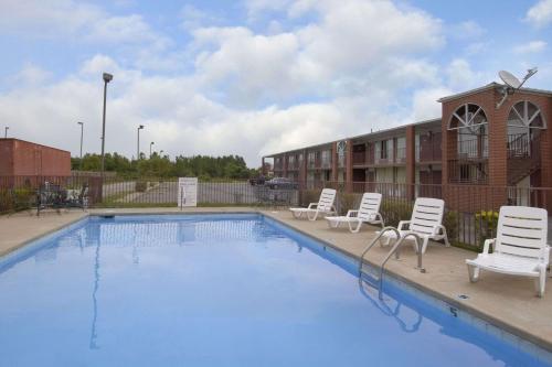 a swimming pool with white chairs next to a building at Days Inn by Wyndham Jonesboro AR in Jonesboro