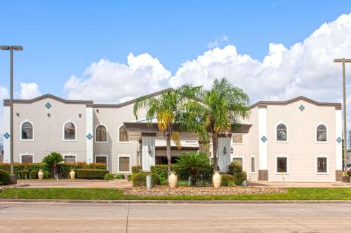 a large white building with palm trees in front of it at Days Inn & Suites by Wyndham Webster NASA-ClearLake-Houston in Webster