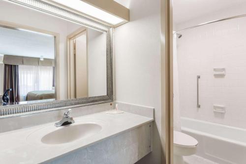 a bathroom with a sink and a toilet and a mirror at Days Inn & Conf Center by Wyndham Southern Pines Pinehurst in Southern Pines