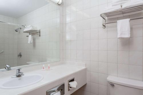 Baño blanco con lavabo y espejo en Days Inn by Wyndham Woodbury Long Island en Woodbury