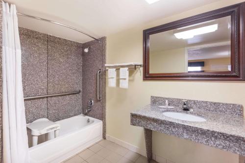 a bathroom with a sink and a tub and a mirror at Days Inn & Suites by Wyndham Warner Robins Near Robins AFB in Warner Robins