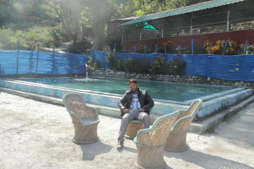 a man sitting in chairs in front of a swimming pool at Natural Camps with InHouse Swimming Pool in Rishīkesh