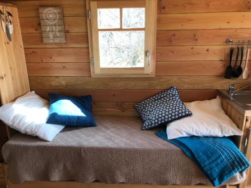 Una cama en una cabaña de madera con almohadas. en La roulotte au fond du pré, en Coltines