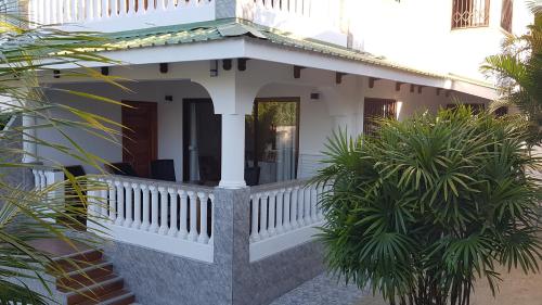 a white house with a porch and palm trees at Drake Seaside Studio Apartments in Bel Ombre