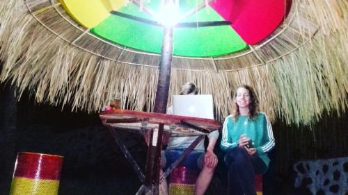 a woman is sitting under a thatched umbrella at Mahoni Guest House in Kelimutu