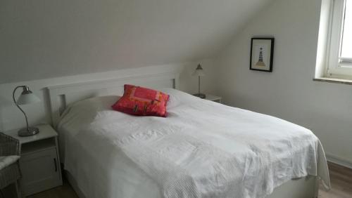 ein weißes Bett mit einem roten Kissen darüber in der Unterkunft Haus Nautilus in Helgoland
