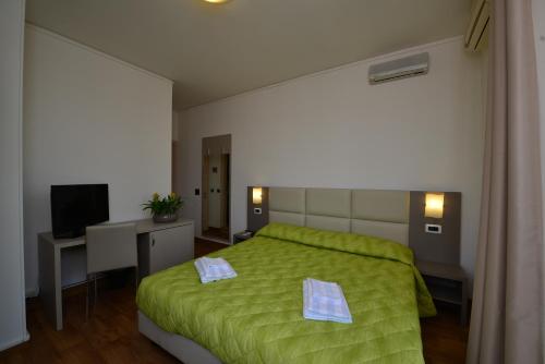 ペスキエーラ・デル・ガルダにあるHotel Bella Peschieraの緑色のベッド、デスク、テレビが備わるベッドルーム1室が備わります。