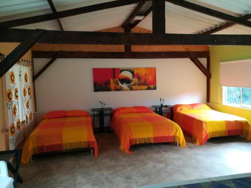 Habitación con 3 camas con colchas de color naranja y amarillo en Hotel Campestre El Refugio de Balsora, en Filandia