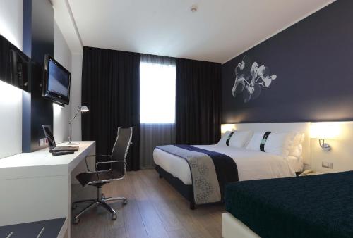 a hotel room with a bed and a desk with a computer at Holiday Inn Milan Nord Zara by IHG in Cinisello Balsamo