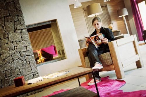 a woman reading a book in a living room with a fireplace at Résidence Les Grandes Feignes in La Bresse