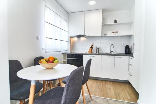 a kitchen with white cabinets and a table with a bowl of fruit at Perla Residence Hotel & SPA in Podgorica