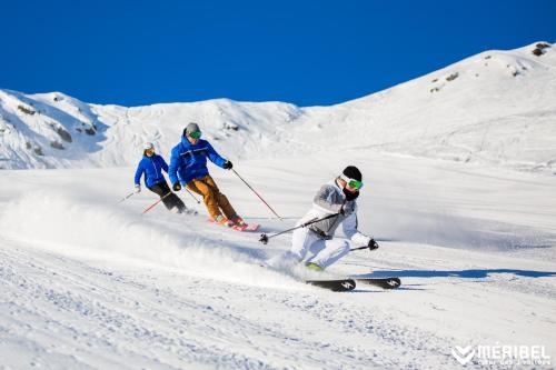 3 personnes font du ski sur une piste enneigée dans l'établissement Hôtel Le Chamois d'Or, USSIM Vacances Méribel, à Méribel