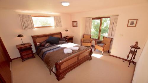 a bedroom with a bed and a chair and windows at Santosha Glade near the Everglades in Leura