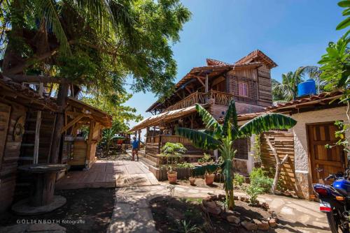 een man die voor een houten huis staat bij Mano a Mano Eco Hostal in Las Peñitas