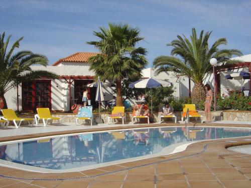 einen Pool in einem Resort mit Stühlen und Palmen in der Unterkunft Bungalows Castillo Beach in Caleta de Fuste
