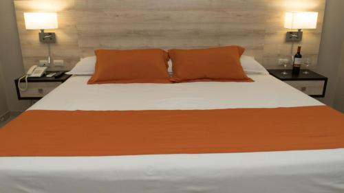 a bed with orange and white sheets and a phone at Hotel Los Almendros in Manta