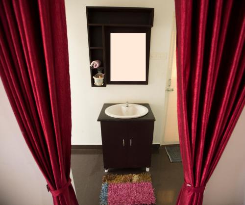 ein Badezimmer mit roten Vorhängen, einem Waschbecken und einem Spiegel in der Unterkunft Green Garden Resort in Kuttālam