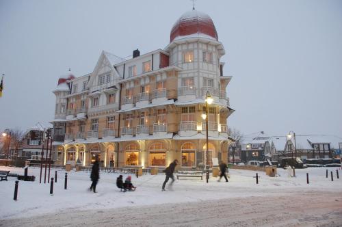 een groot gebouw met mensen ervoor in de sneeuw bij Grand Hotel Belle Vue in De Haan