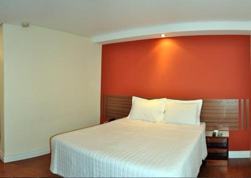 um quarto com uma cama branca e uma parede laranja em Hotel Vollare em Osasco