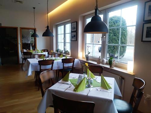 un restaurante con mesas y sillas blancas y ventanas en Hotel Am Meilenstein, en Dunkelforth