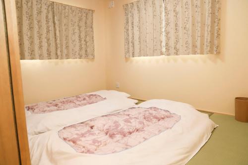 two beds in a room with two windows at Guest House En in Nara