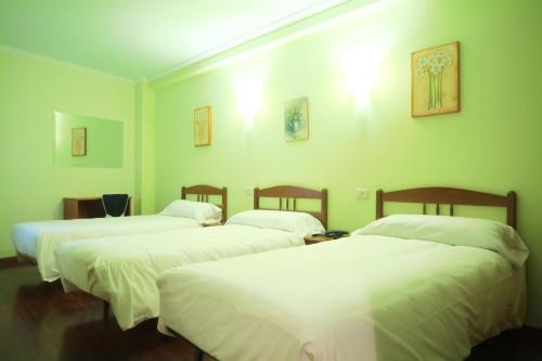 three beds in a room with green walls at Hotel Camiño do Mar in Urdilde