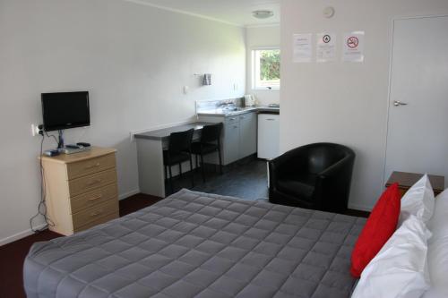 a bedroom with a bed and a desk and a kitchen at Burgundy Rose Motel in Whangarei