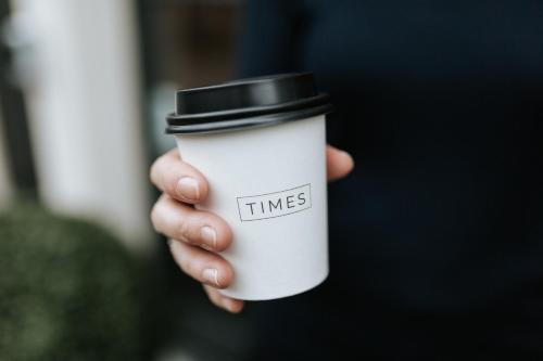 a hand holding a white coffee cup with a black top at The Times Hotel in Amsterdam