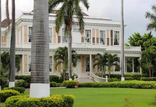 a large white house with palm trees in front of it at Artist Place Kensington 2BR New Kingston in New Kingston