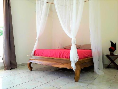 a bedroom with a bed with red sheets and white curtains at Villa BonBon Siwo in Le Diamant