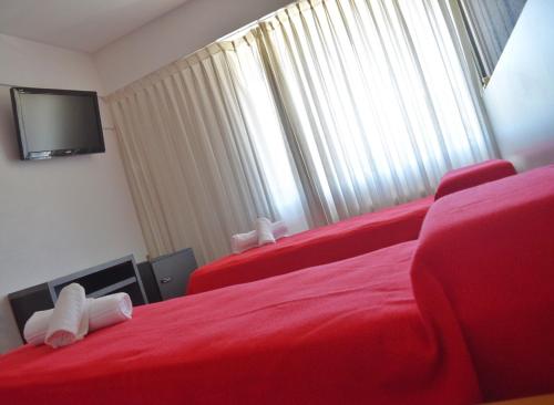 a bedroom with two red beds and a flat screen tv at Hotel Don Carlos in Villa Gesell