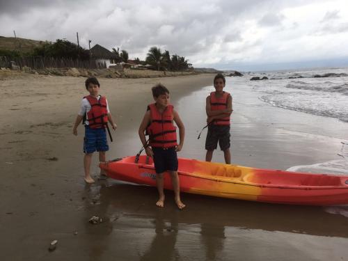three boys are standing next to a canoe on the beach at Baja Canoas Hotel in Canoas De Punta Sal