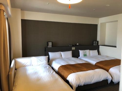 a hotel room with two beds with white sheets at Dormy Inn Nagasaki Shinchichukagai in Nagasaki