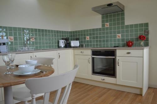 a kitchen with white cabinets and a table with chairs at The Pigsty in Ashbourne