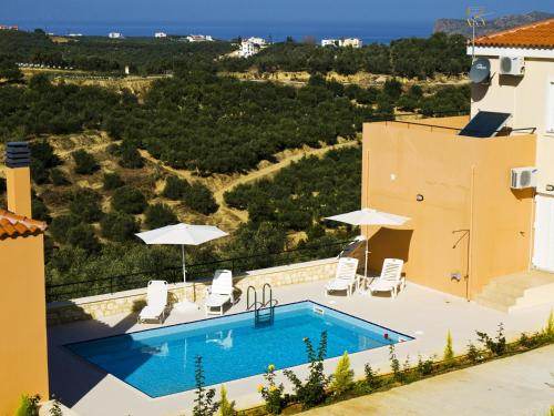 a pool on the side of a building with chairs and umbrellas at Olive Tree Hillside Apartment in Stalos