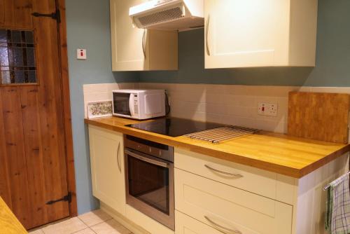 a kitchen with white cabinets and a microwave at The Buttery at Trussel Barn in Liskeard