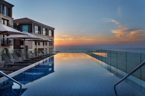 a swimming pool with chairs and the ocean at sunset at The Setai Tel Aviv, a Member of the leading hotels of the world in Tel Aviv
