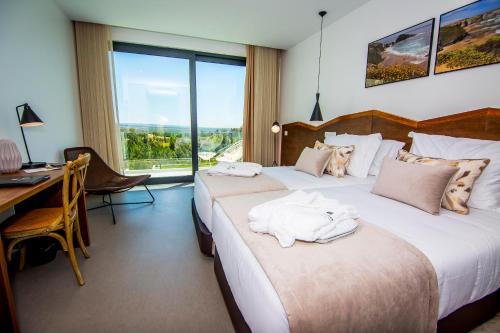 a hotel room with two beds and a desk and a window at Enigma - Nature & Water Hotel in São Teotónio